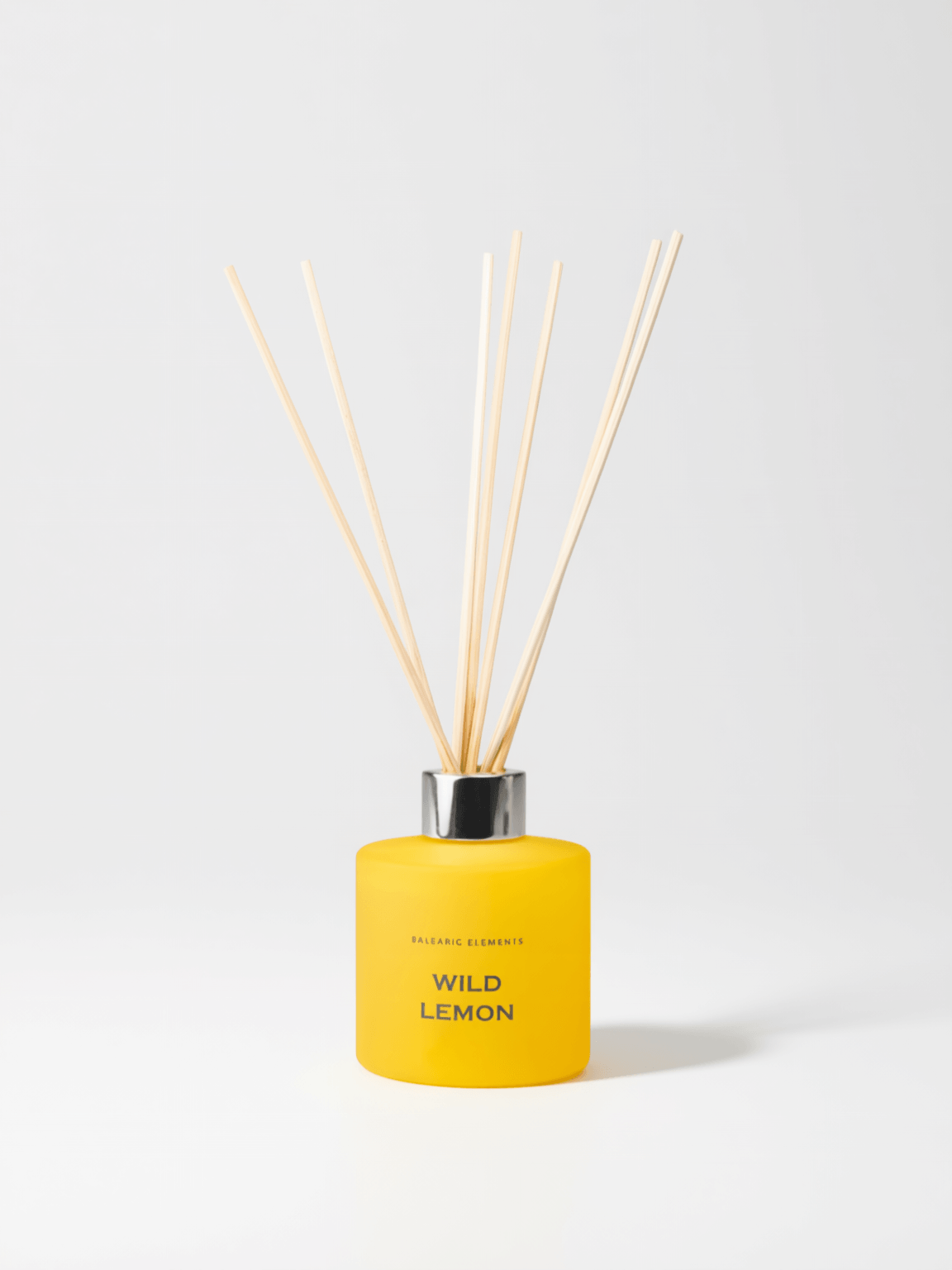 A yellow reed diffuser bottle with natural wooden reeds, labeled 'WILD LEMON' by Balearic Elements, on a clean white background.