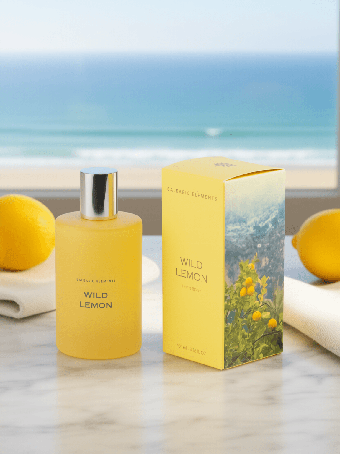 A yellow Balearic Elements Wild Lemon fragrance bottle stands next to its matching yellow box on a marble surface, with lemons and a blurred ocean view in the background.