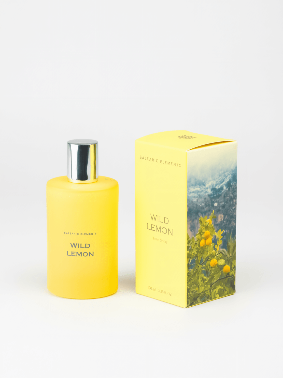 A yellow bottle of Wild Lemon Room Spray by Balearic Elements stands next to its matching yellow packaging box featuring a lemon and mountain landscape illustration, set against a plain white background.
