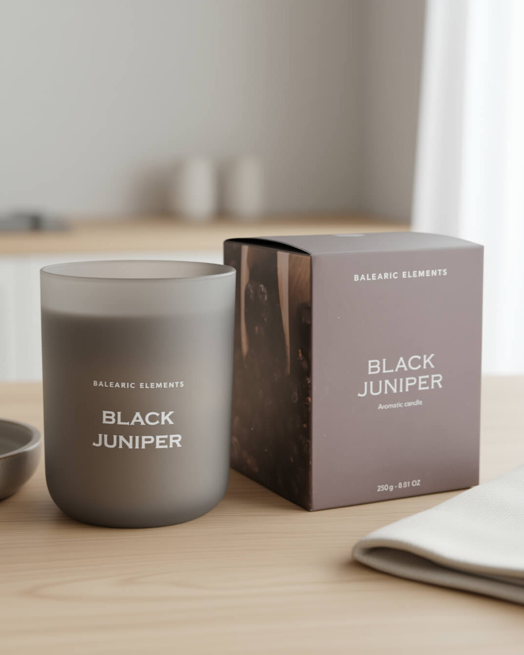 Smokey grey candle labeled 'Black Juniper' next to its packaging on a wooden surface.