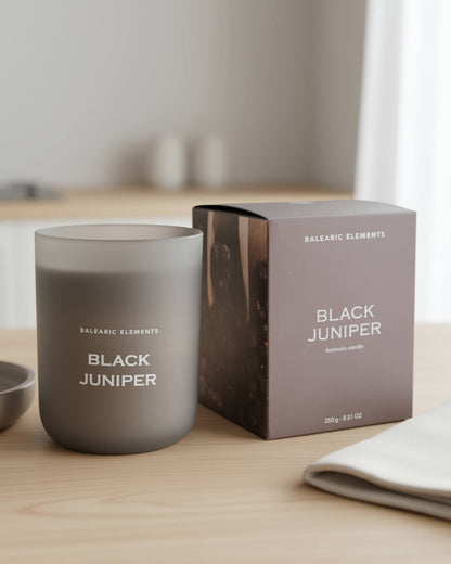 Smokey grey candle labeled 'Black Juniper' next to its packaging on a wooden surface.