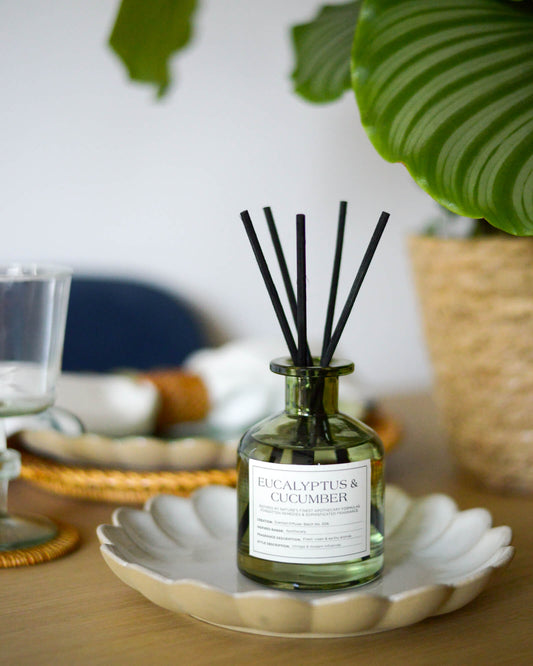 Light greend diffuser bottle labeled 'Eucalyptus & Cucumber' on a decorative plate with plants in the background