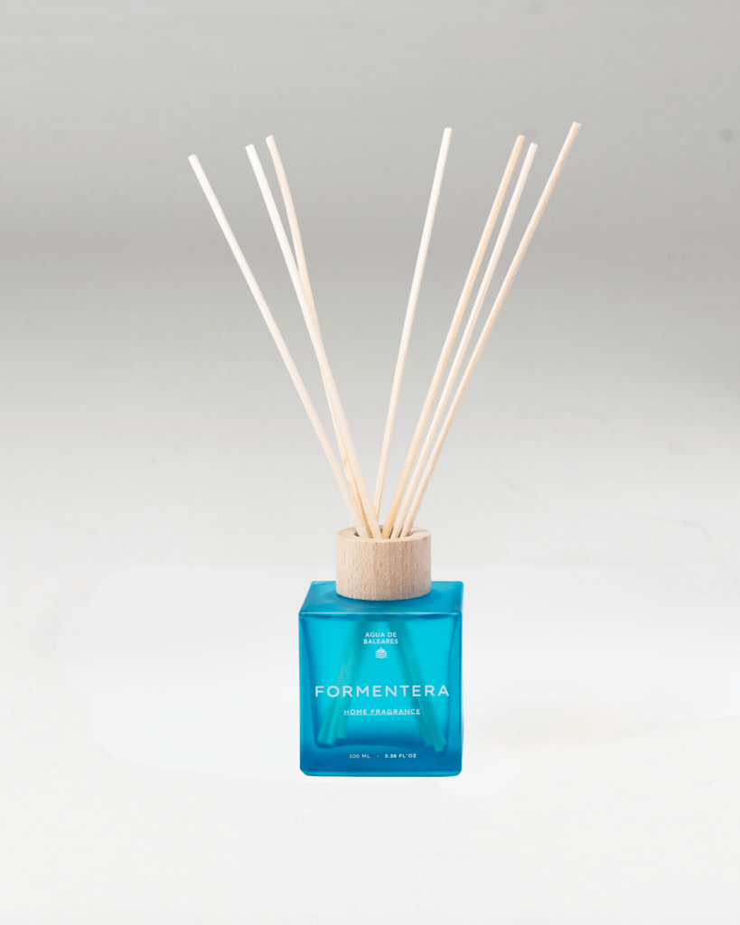 A reed diffuser bottle with a translucent blue glass base, a light wood cap, and natural reed sticks, labeled FORMENTERA on a light gray background.
