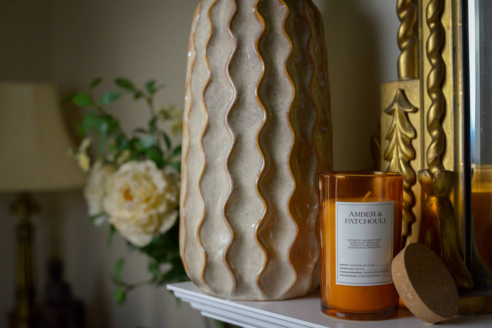 Candle with wavy textured vase and decorative items on a mantlepiece