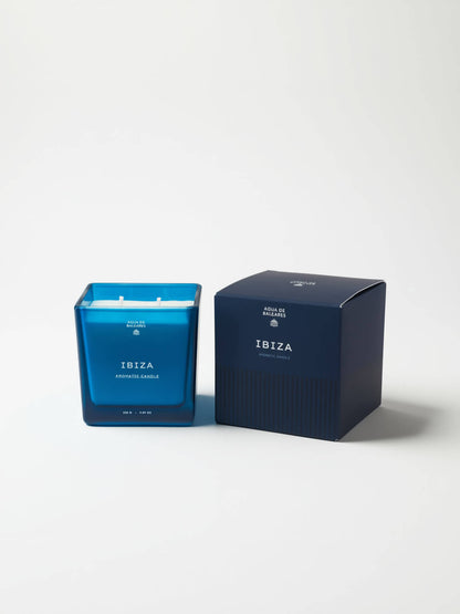 A blue glass jar candle next to its dark navy blue packaging box, both featuring the scent name 'IBIZA'  on a clean white background.