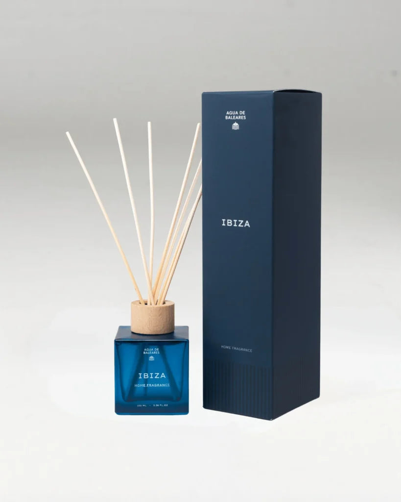 An Ibiza reed diffuser set with a blue glass bottle, natural wood reeds, and a tall navy blue box on a light gray background.