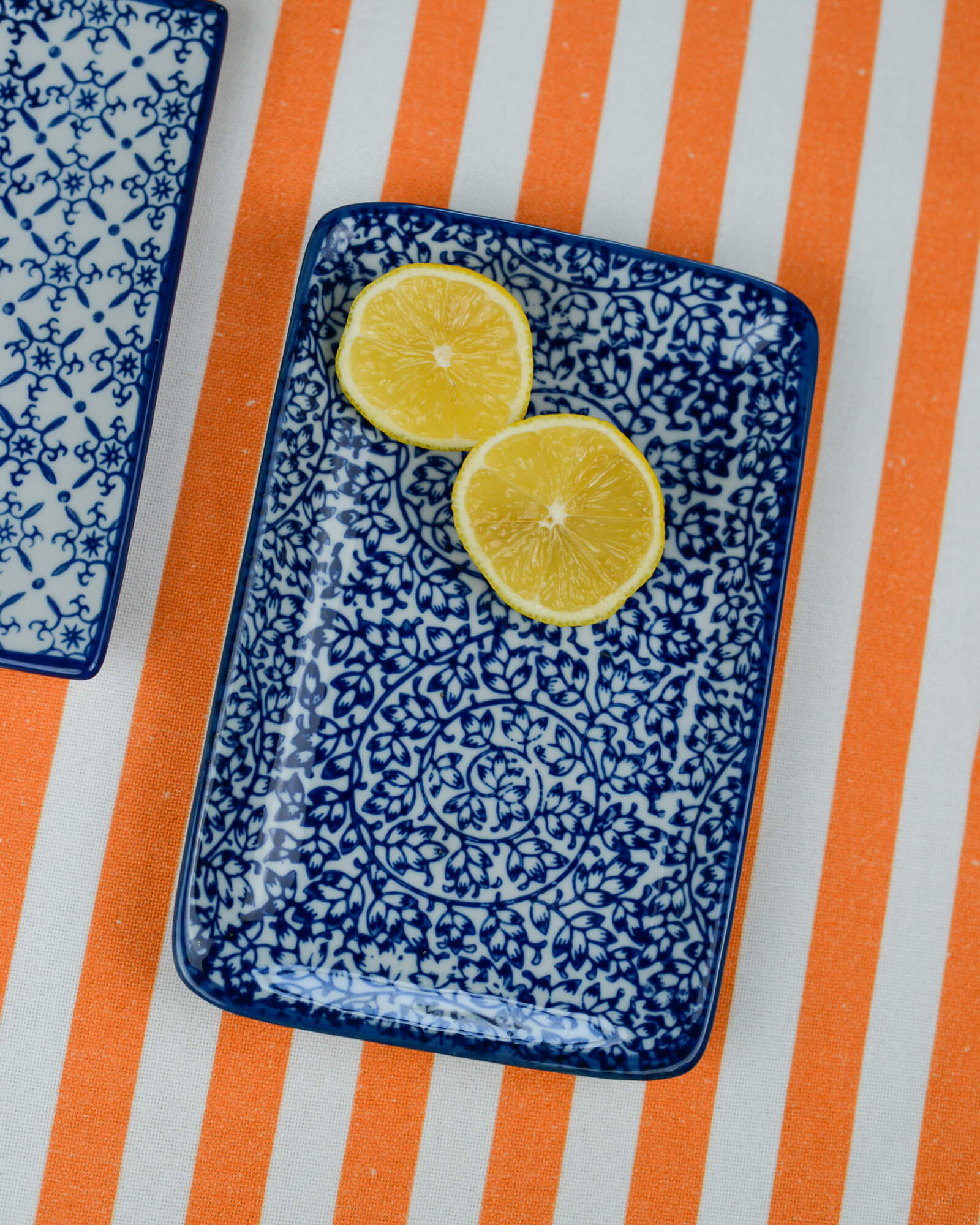 Two lemon slices on a blue patterned rectangular plate with an orange and white striped table runner underneath.