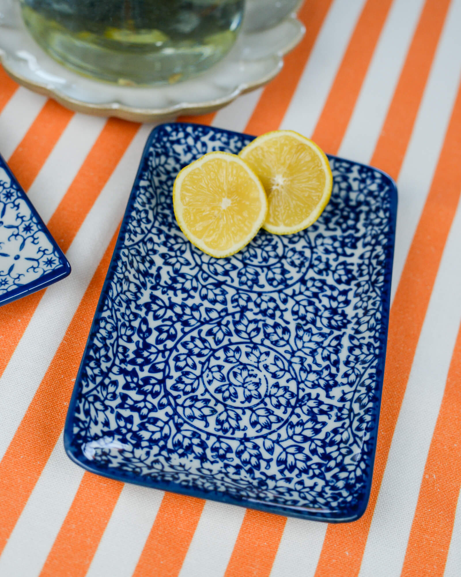 Blue patterned tray with lemon slices on an orange and white striped tablecloth.