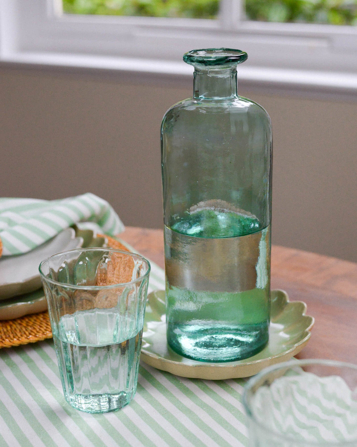 Green glass decorative bottle vase and glass on a table with a striped tablecloth