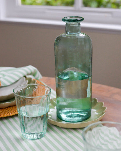 Green glass decorative bottle vase and glass on a table with a striped tablecloth