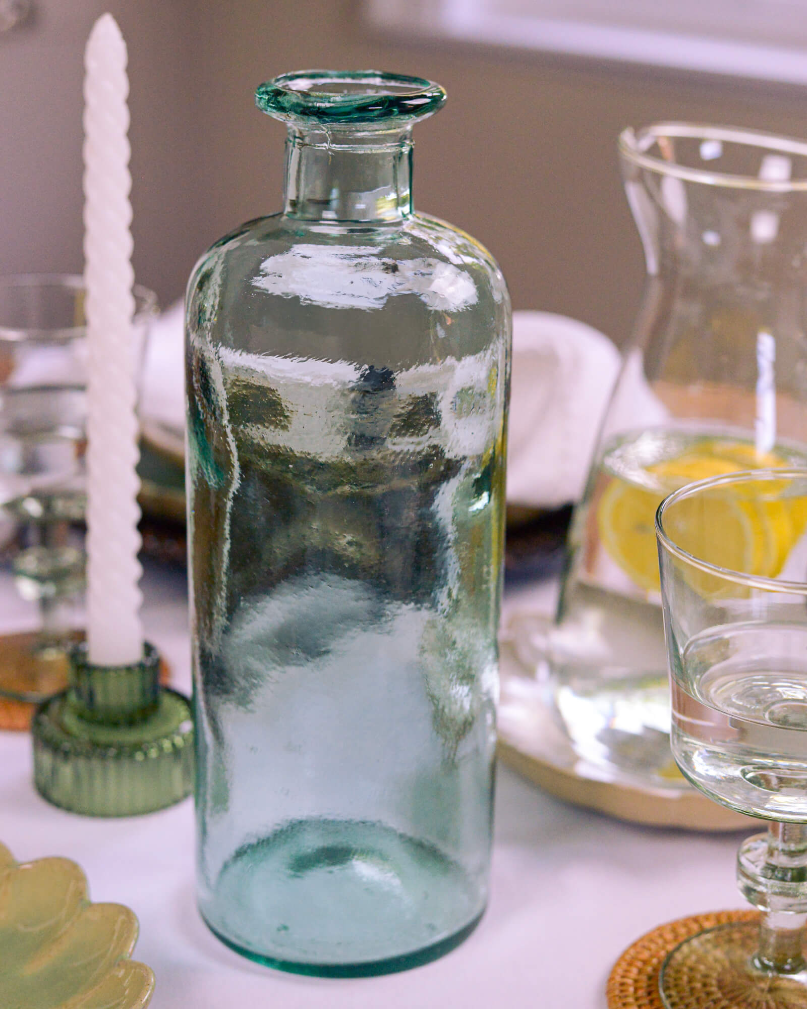 Clear glass bottle on a table with candles and glasses in the background