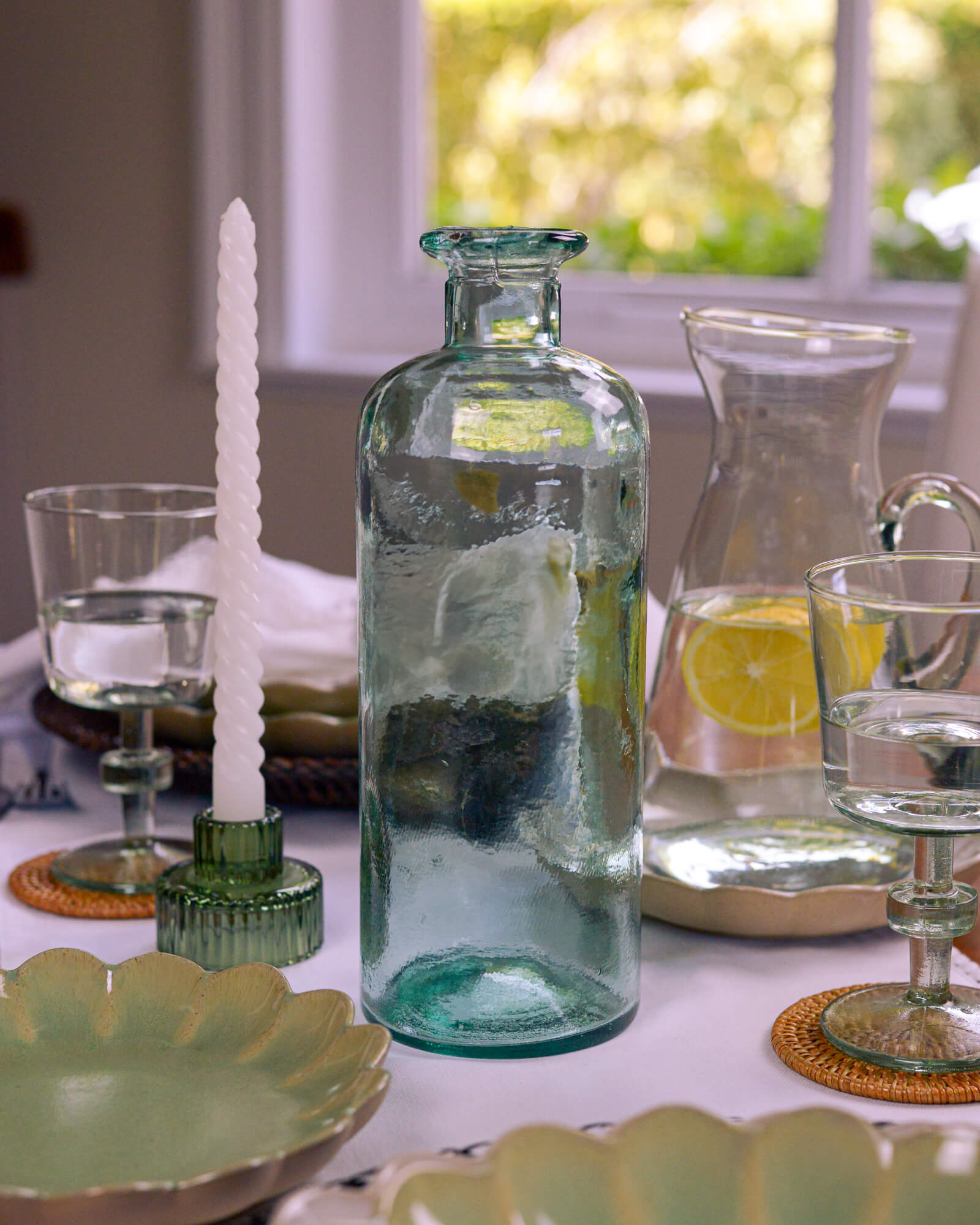 Decorative table setting with a glass bottle, candle, and lemon on a table.