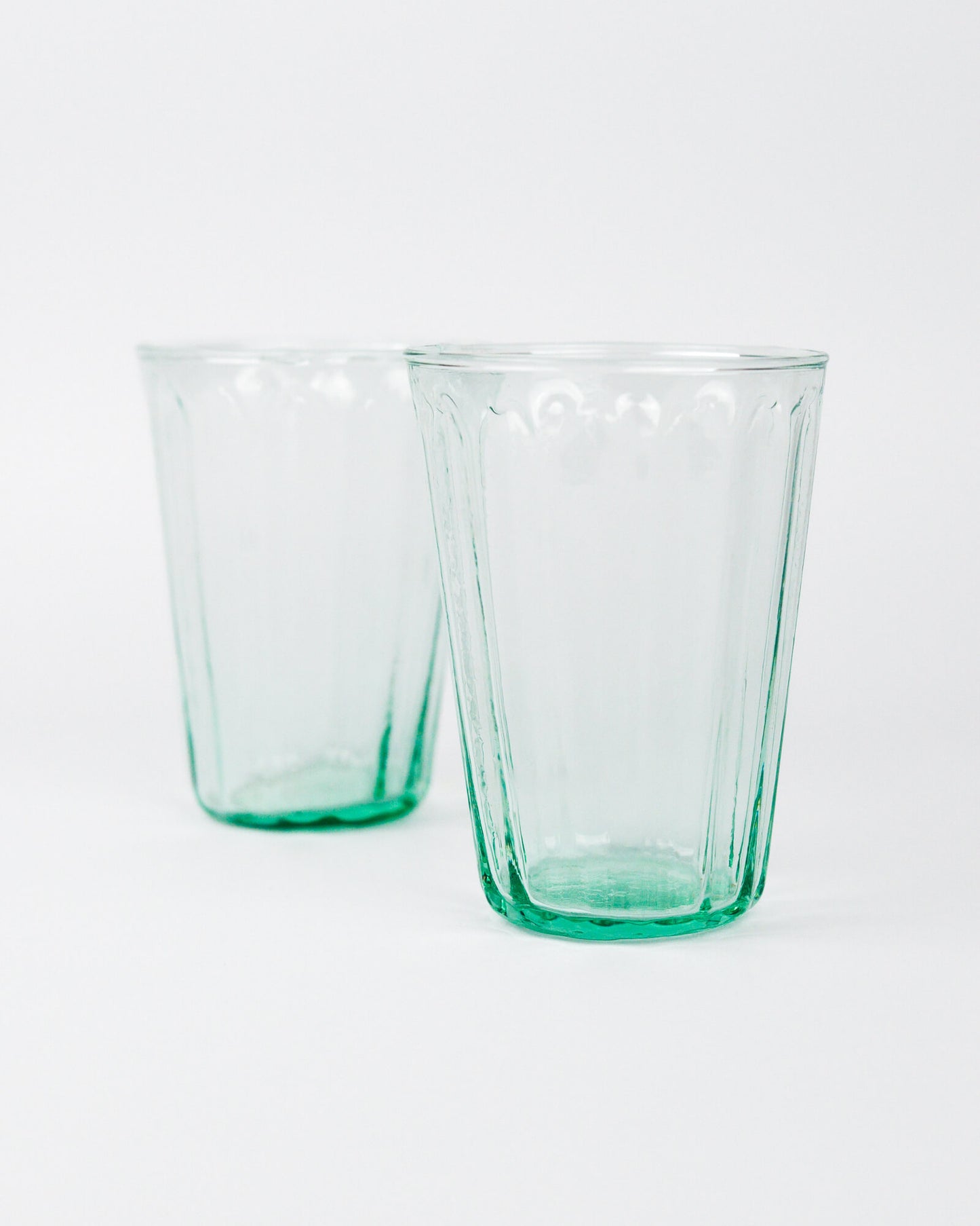 Two green glass tumblers on a white background