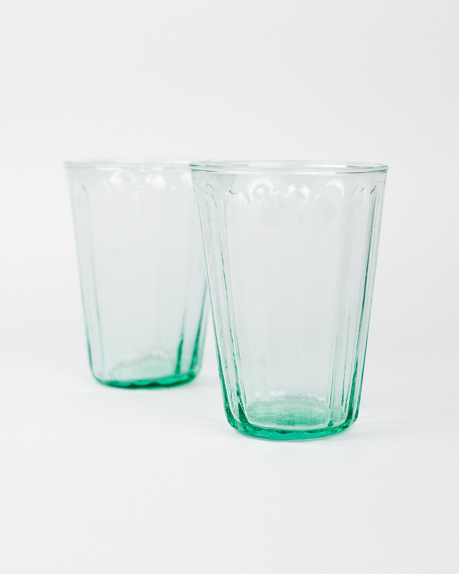 Two green glass tumblers on a white background