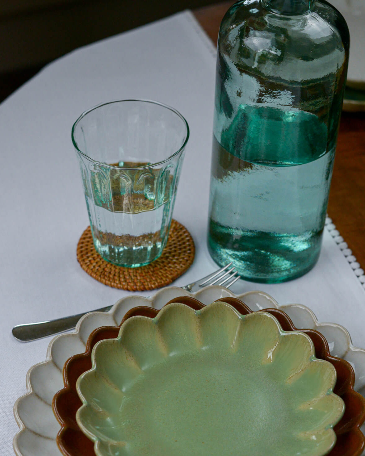Green glass bottle and green glass tumbler on a table with a plate and fork.