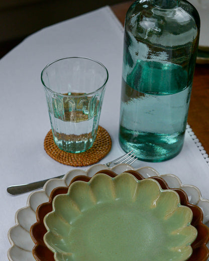 Green glass bottle and green glass tumbler on a table with a plate and fork.