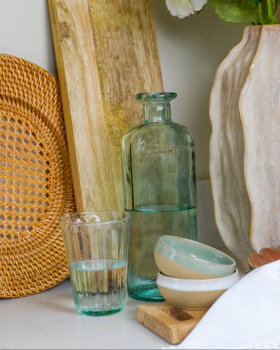 Decorative setting with a glass tumbler, green bottle, and ceramic items on a surface.