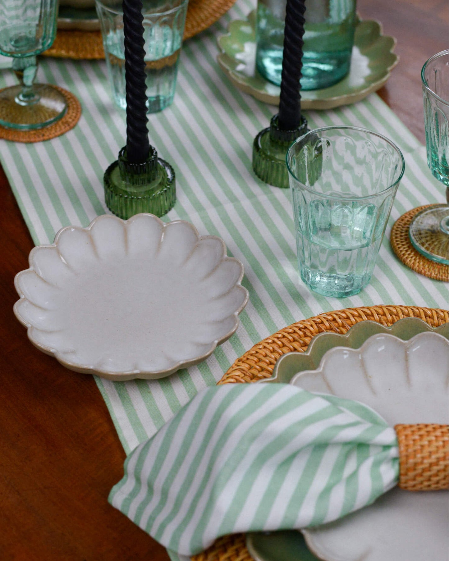 Table setting with green and white striped table runner, white plates, and decorative napkins.