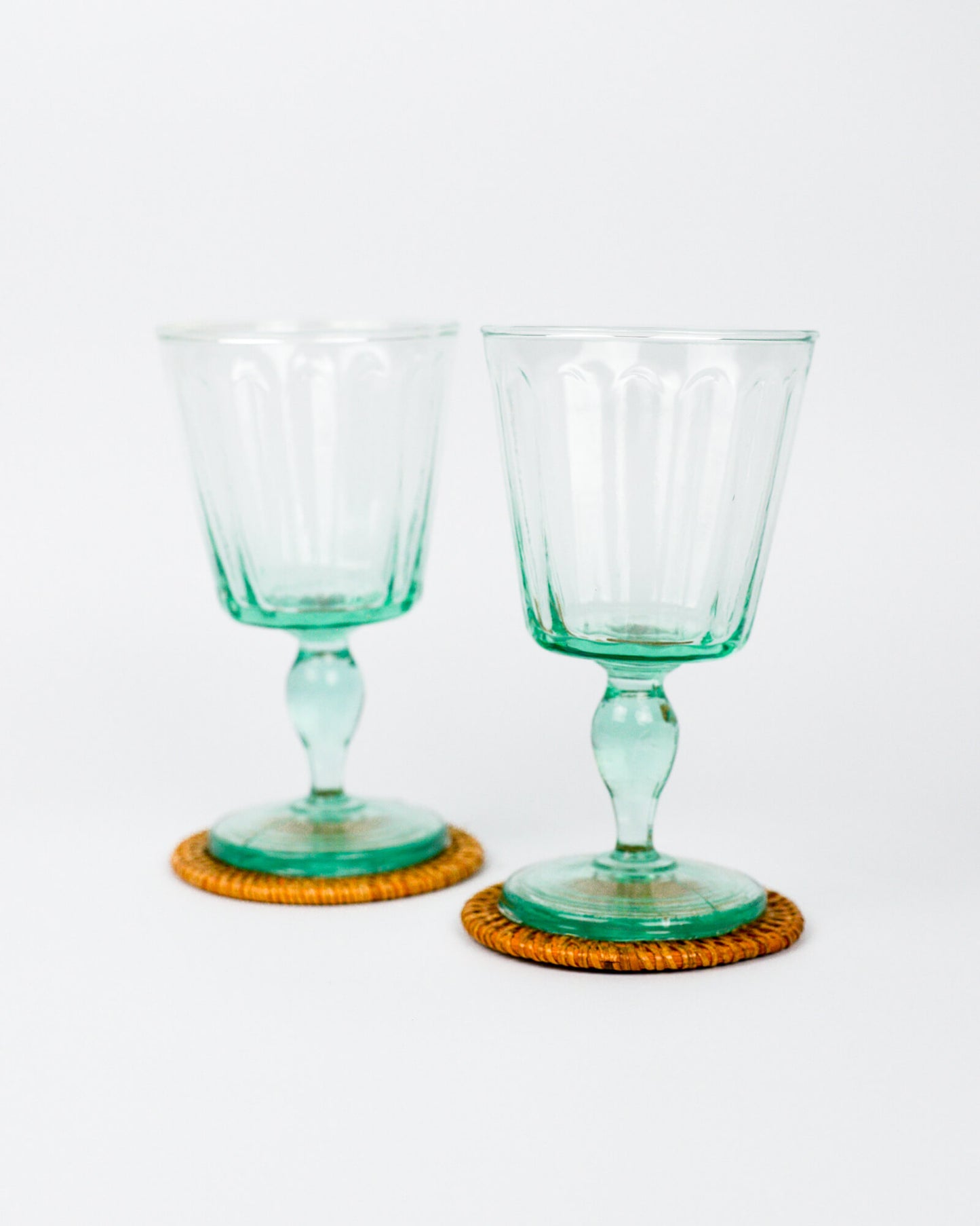 Two green glass goblets on orange woven coasters against a white background