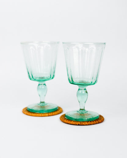 Two green glass goblets on orange woven coasters against a white background