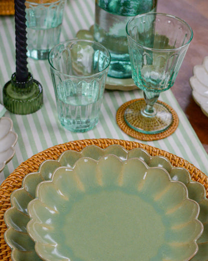 Green ceramic scalloped edge plate on a woven placemat with striped tablecloth and recycled wineglasses in the background