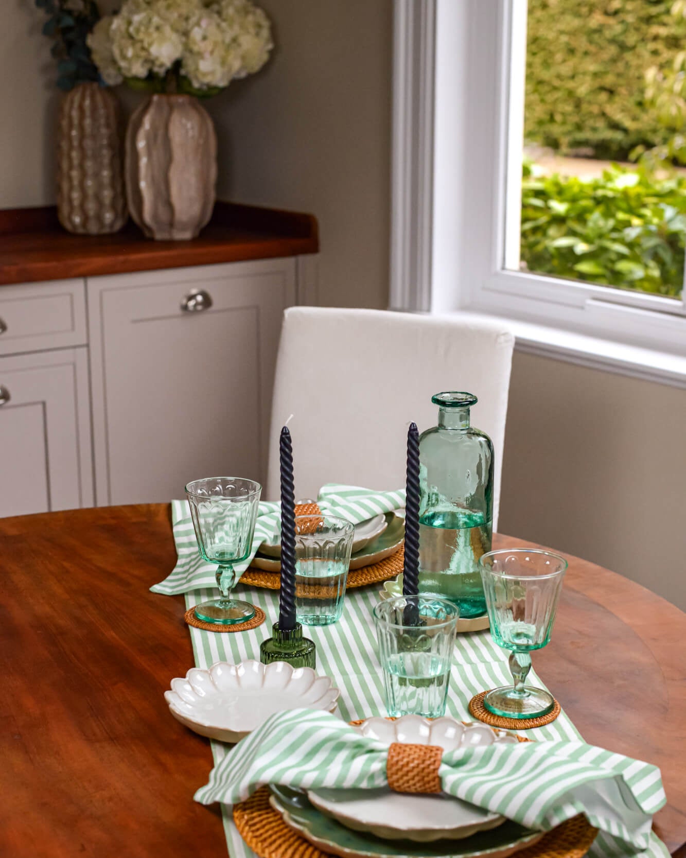 Dining table set with green glasses, striped napkins, and candles in a home setting.