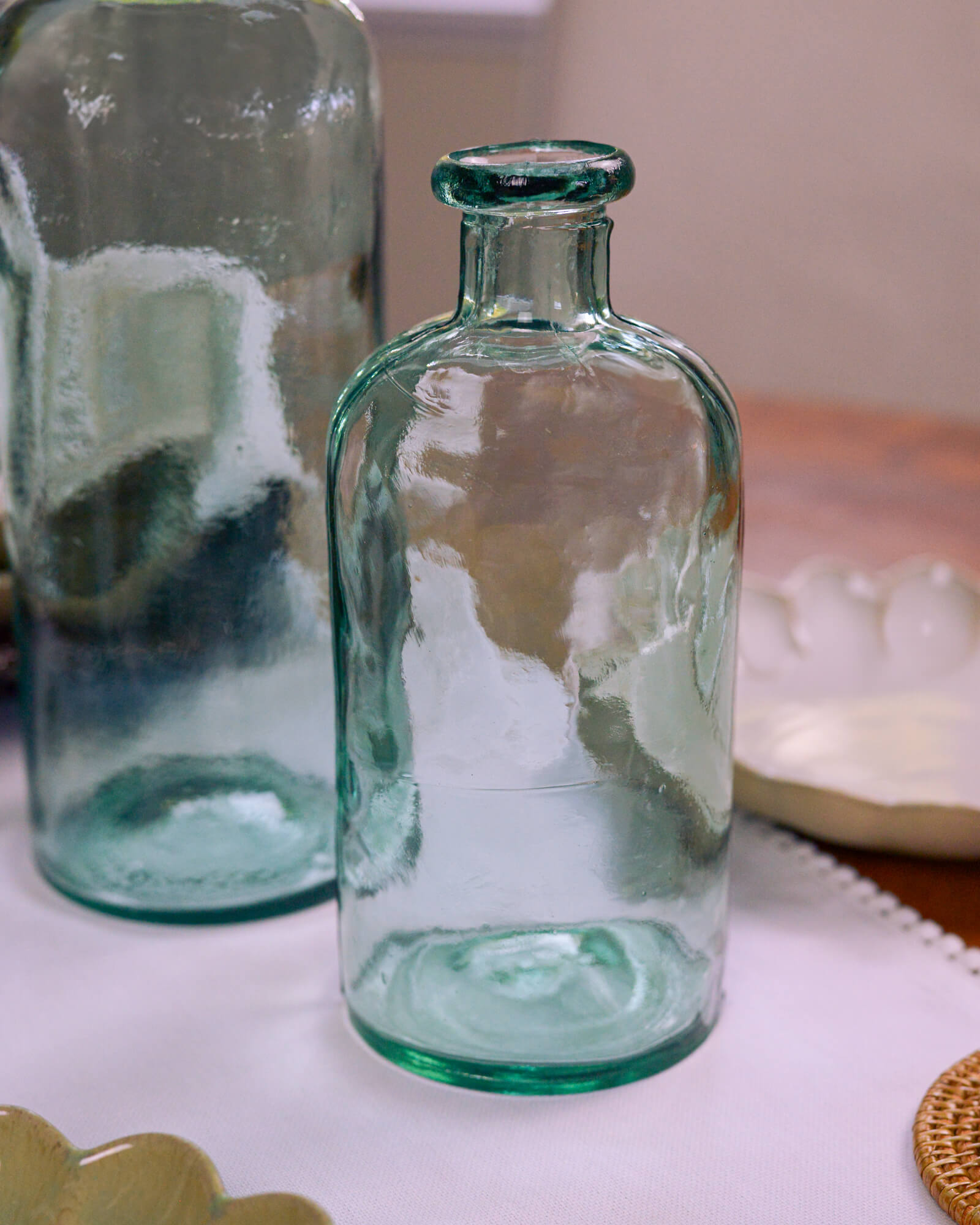 Two green glass bottles on a white cotton table runner