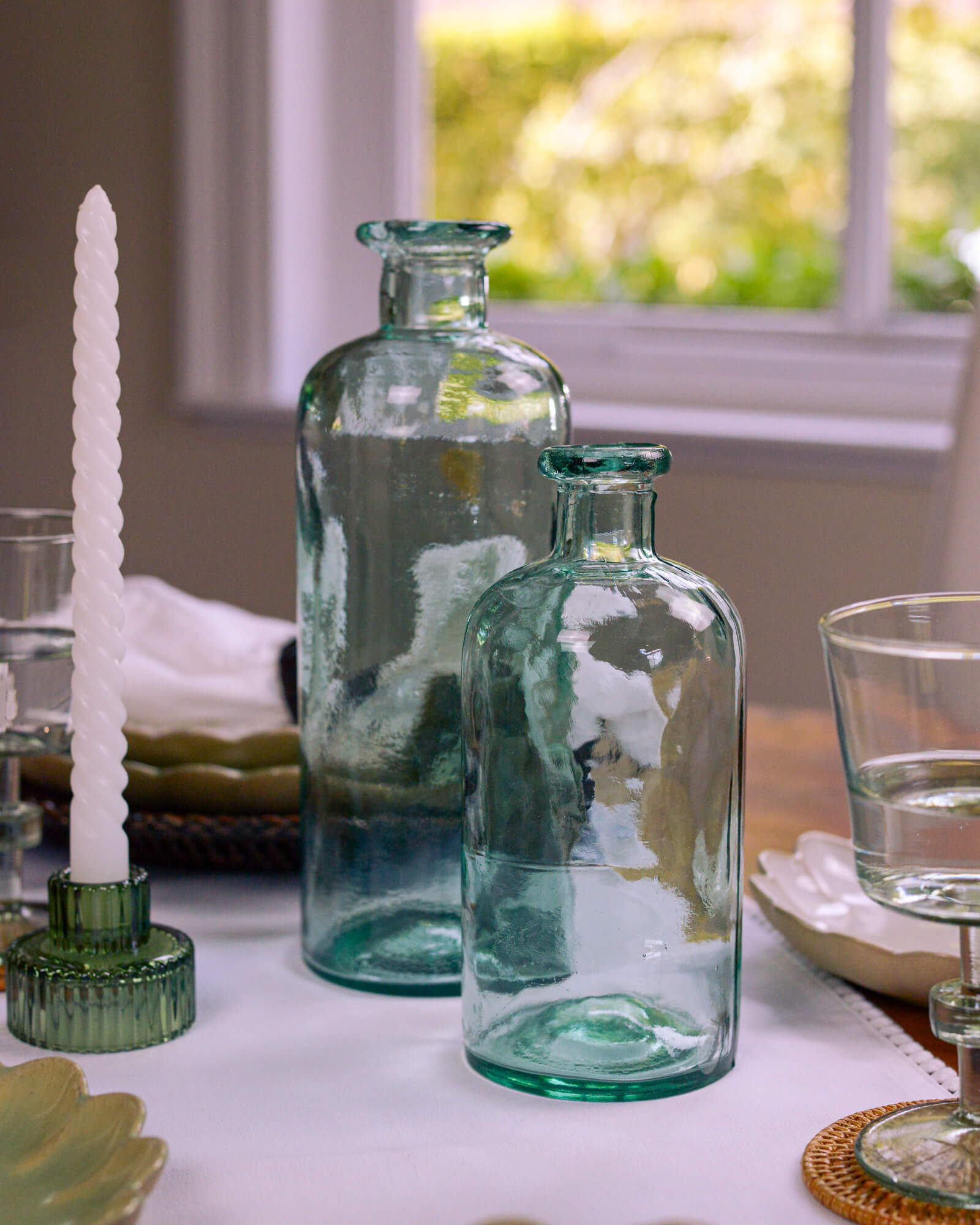 Two green glass bottles on a table with a blurred outdoor background