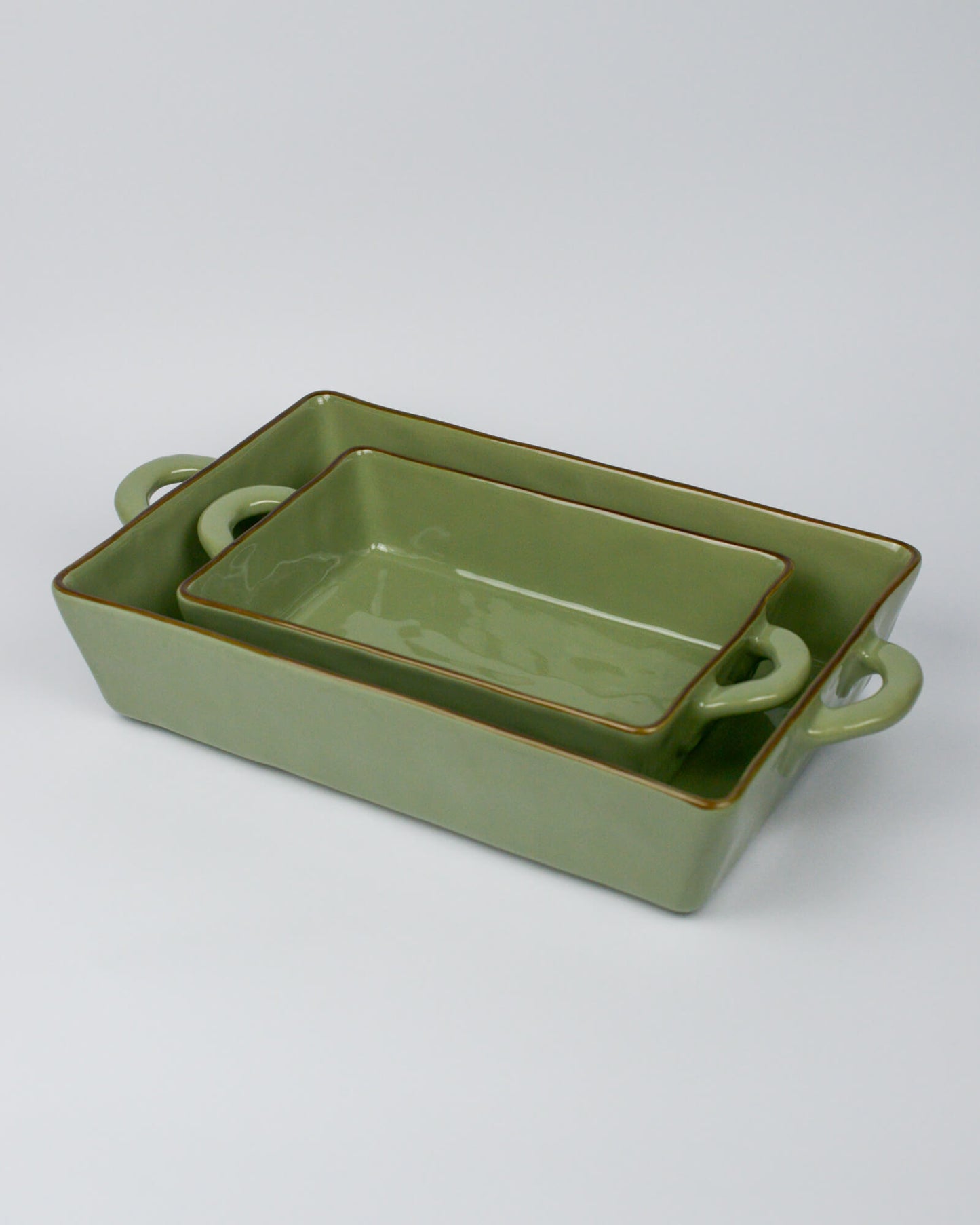 Set of two green ceramic baking dishes with handles on a white background