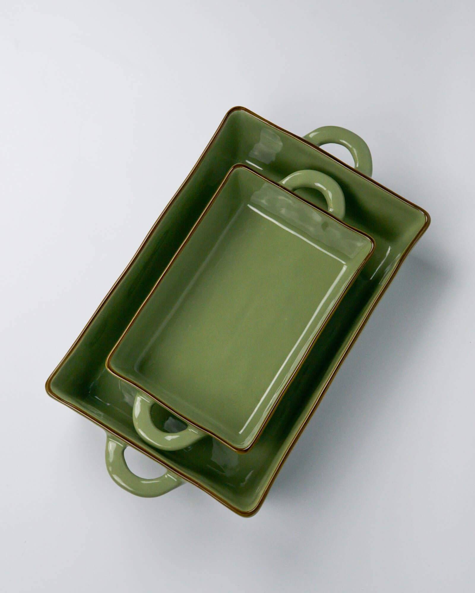 Two green ceramic baking dishes with handles on a white background