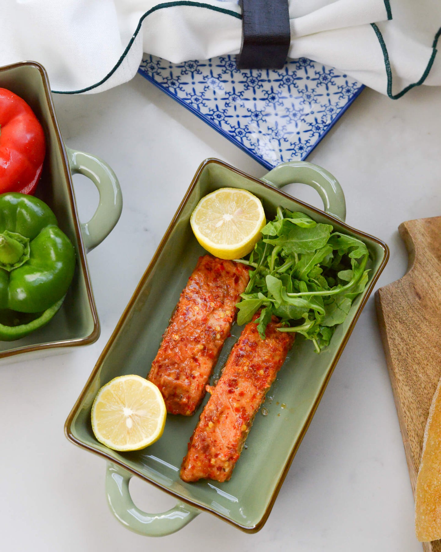 Salmon fillets with lemon and arugula in an olive green rectangular ceramic baking dish.
