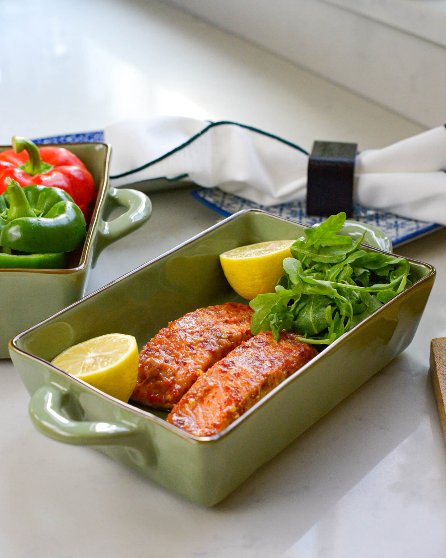 Green baking dish with handles holding salmon, lemon, and salad on a kitchen counter
