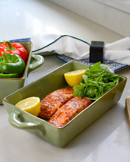 Green baking dish with handles holding salmon, lemon, and salad on a kitchen counter