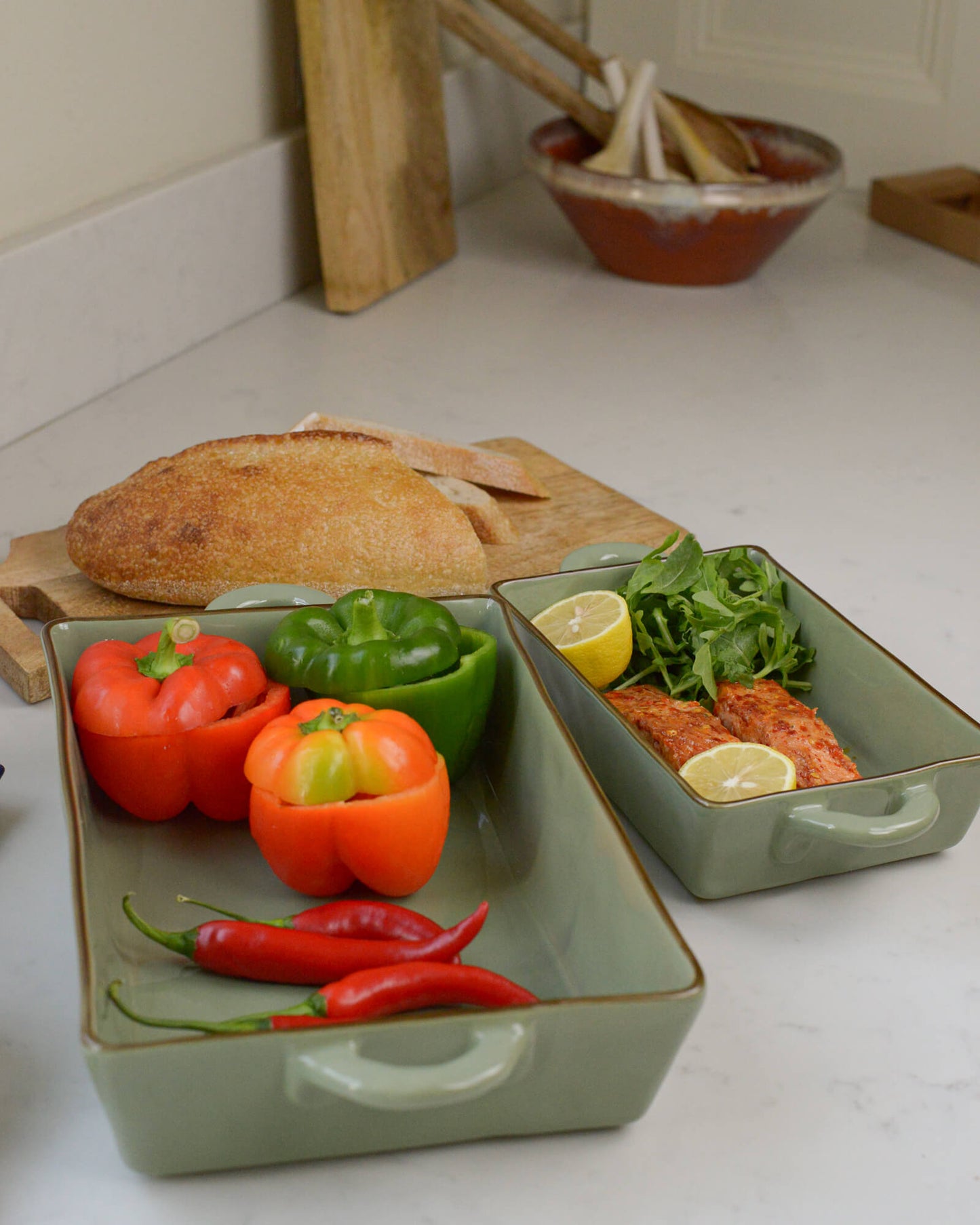 Two olive green ceramic baking dishes with vegetables on a kitchen counter