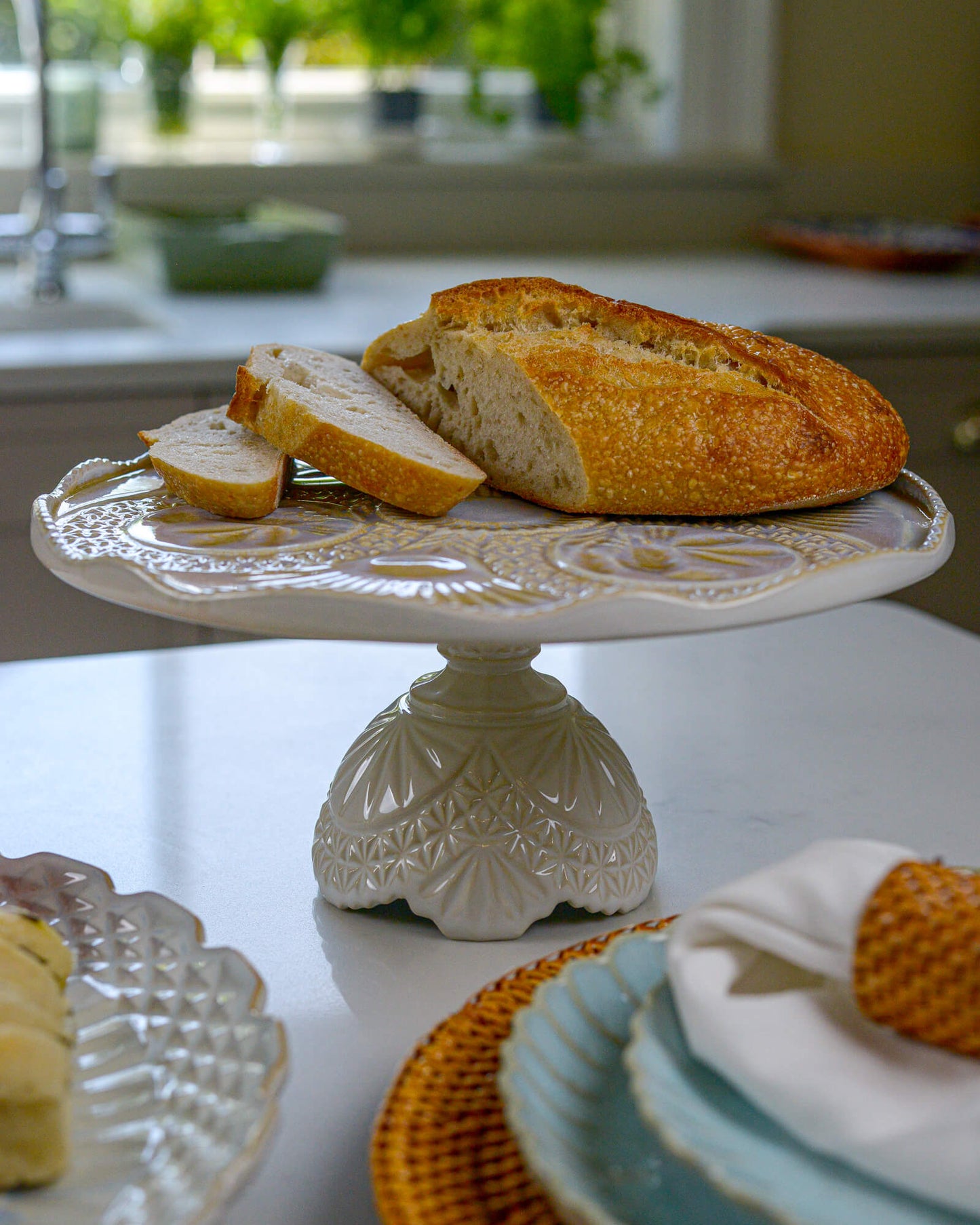Loaf of sourdough bread on a decorative cake stand in a kitchen setting