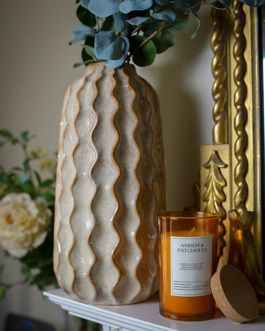 Decorative ceramic vase with wavy pattern on a mantlepiece with orange candle