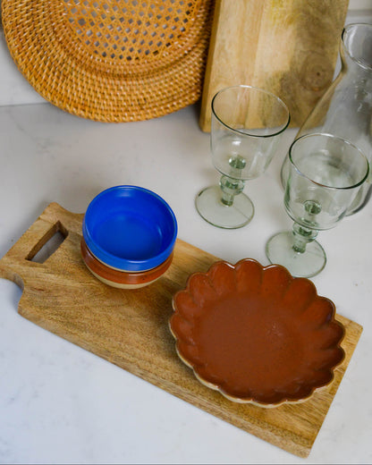 Ceramic bowls and glasses on a wooden grazing paddle with a woven mat in the background.