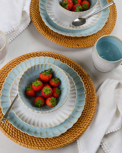Scalloped edged ceramic stoneware cereal bowls layered on rattan charger plates 