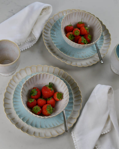 Two ceramic scalloped edge bowls with strawberries on light blue salad plates on a light marble surface with white napkins.