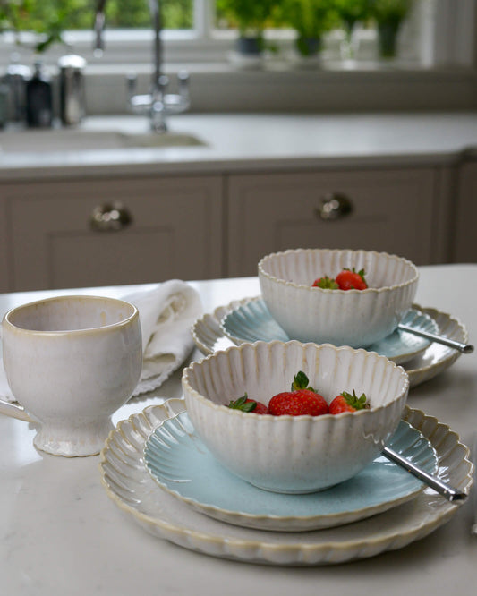 Two cream scalloped edge cereal bowls on a white marble surface 