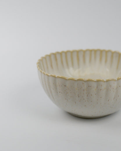 Ceramic bowl with textured surface and scalloped rim on a white background