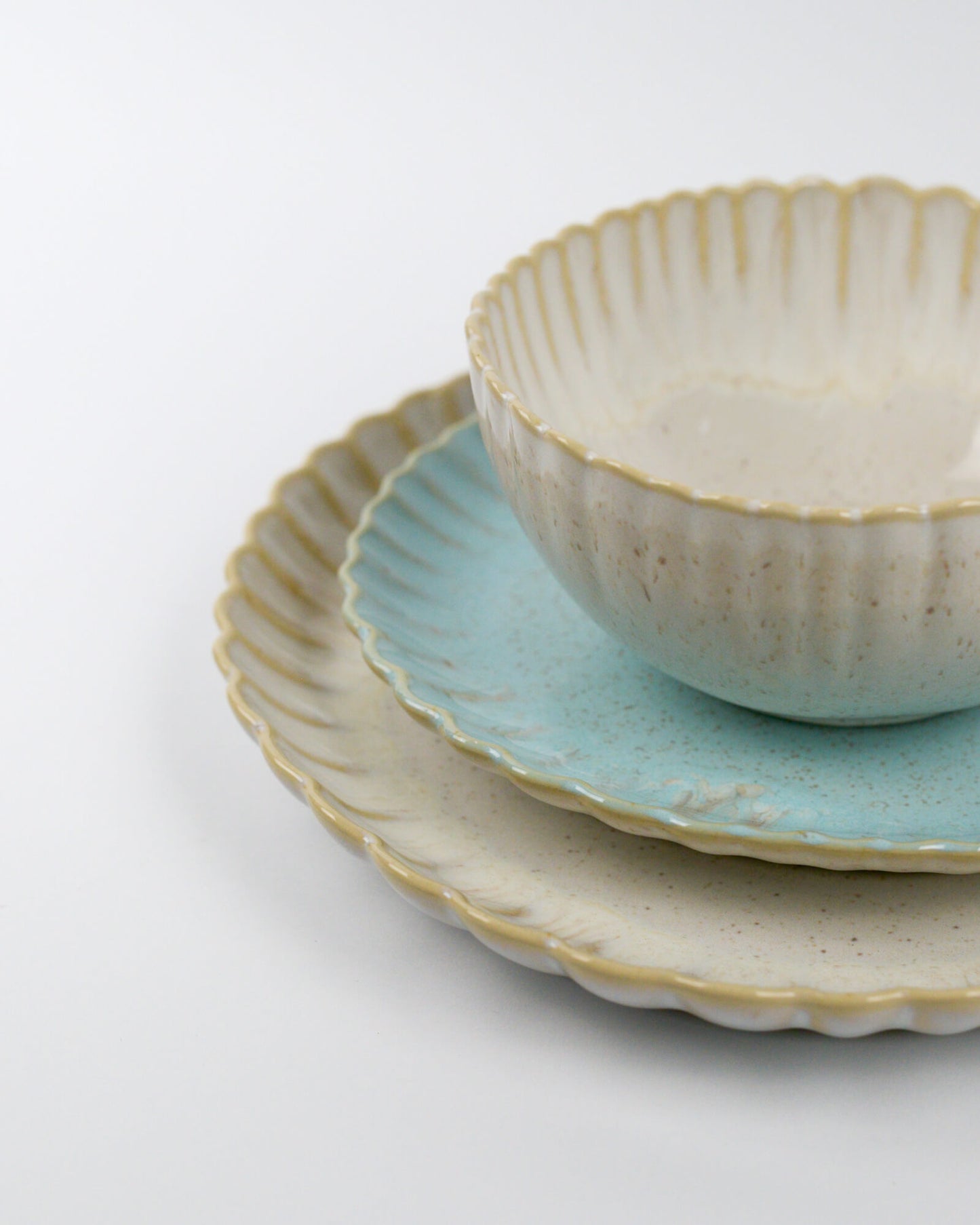 Set of ceramic plates and cereal bowl with scalloped rims on a white background