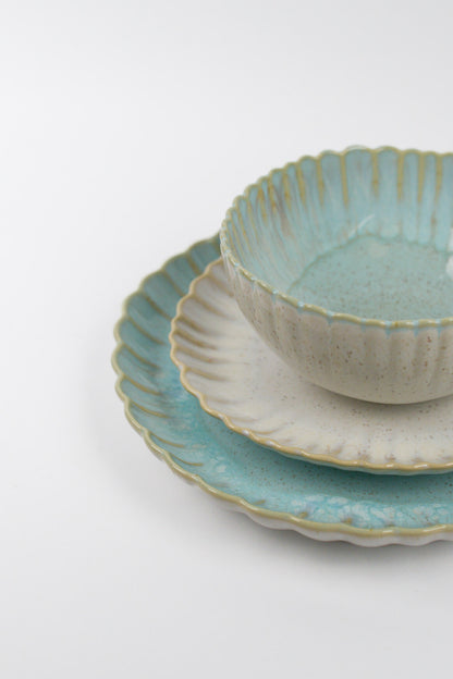 Set of ceramic scalloped edge bowls and plates with textured surfaces on a white background