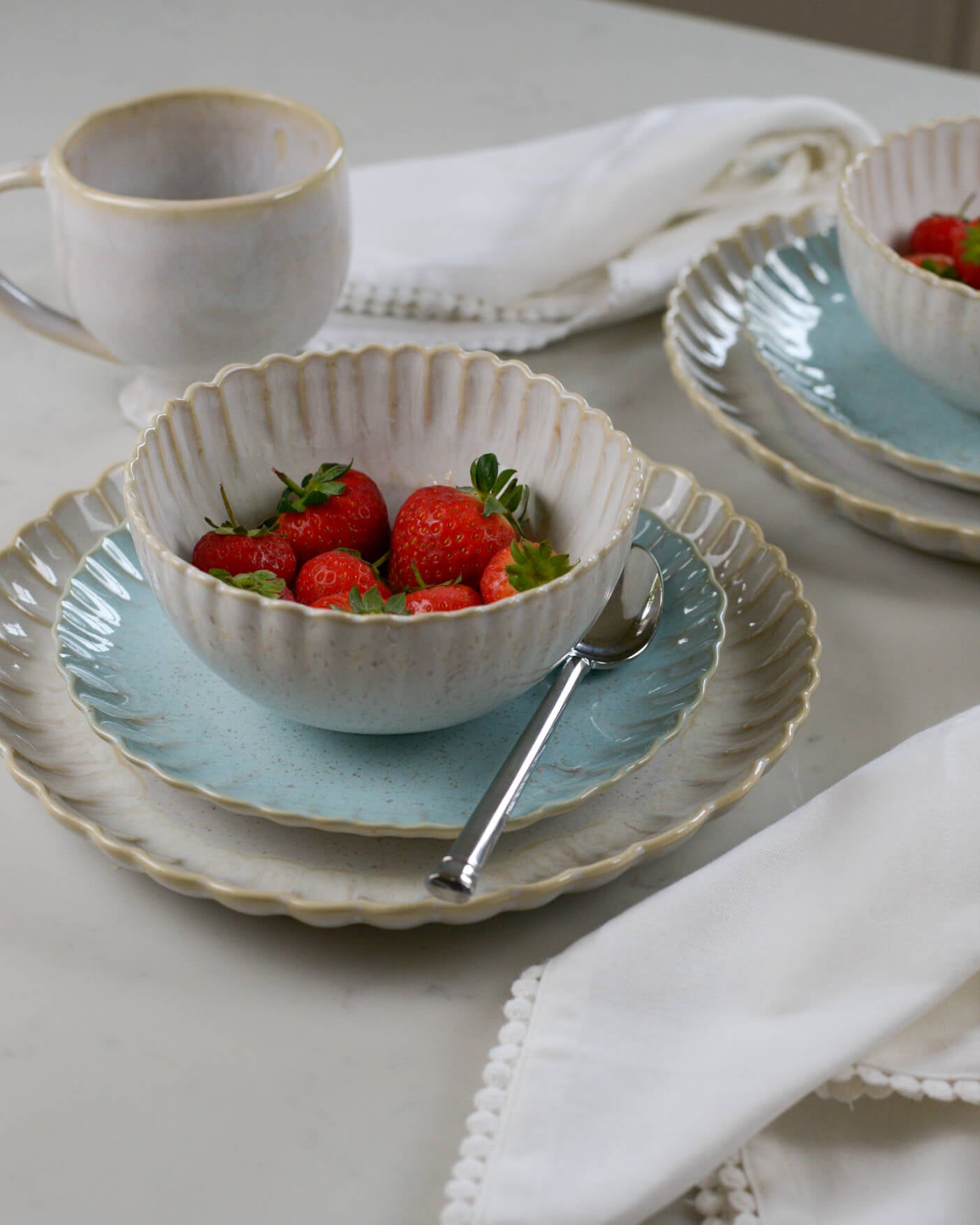 Linen white scalloped edge dinner plate layered with light blue salad plate and scalloped edge breakfast bowl on a marble surface