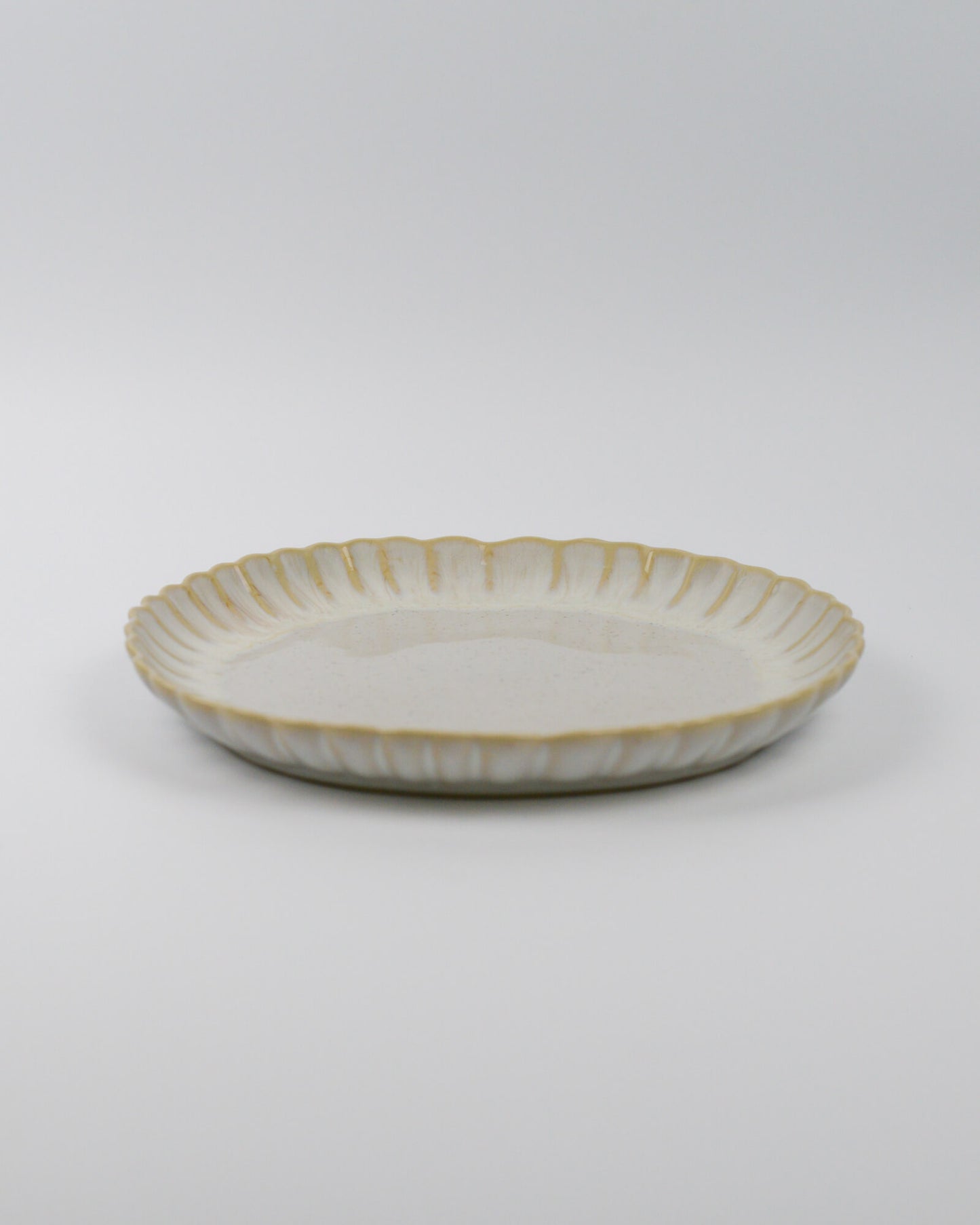 Ceramic stoneware plate with a scalooped edge on a white background
