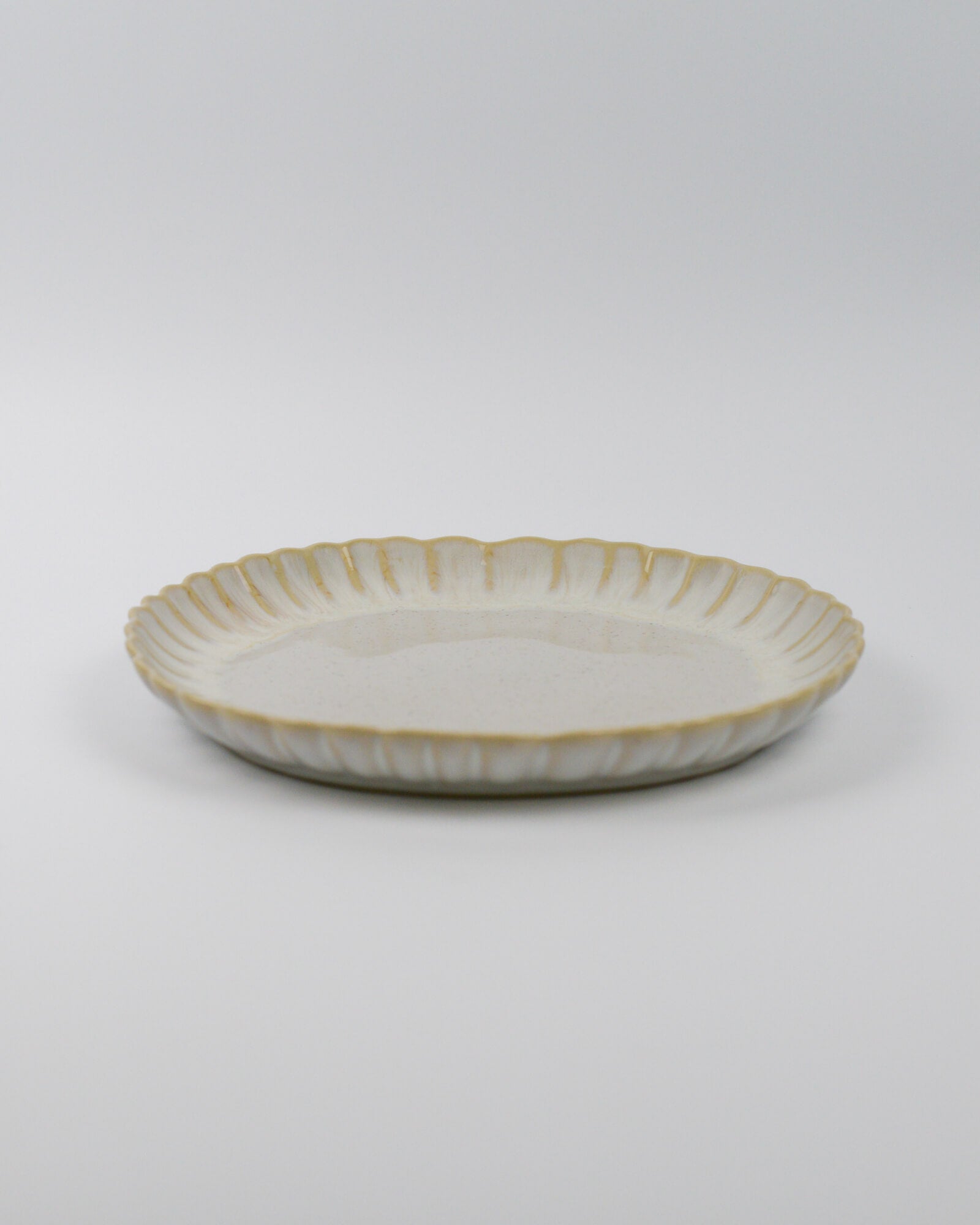 Ceramic stoneware plate with a scalooped edge on a white background
