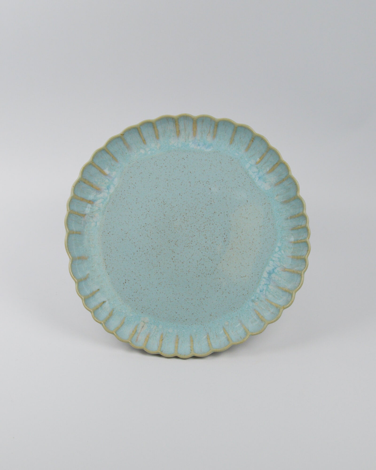 Light blue ceramic stoneware dinner plate with scalloped edge on a white background