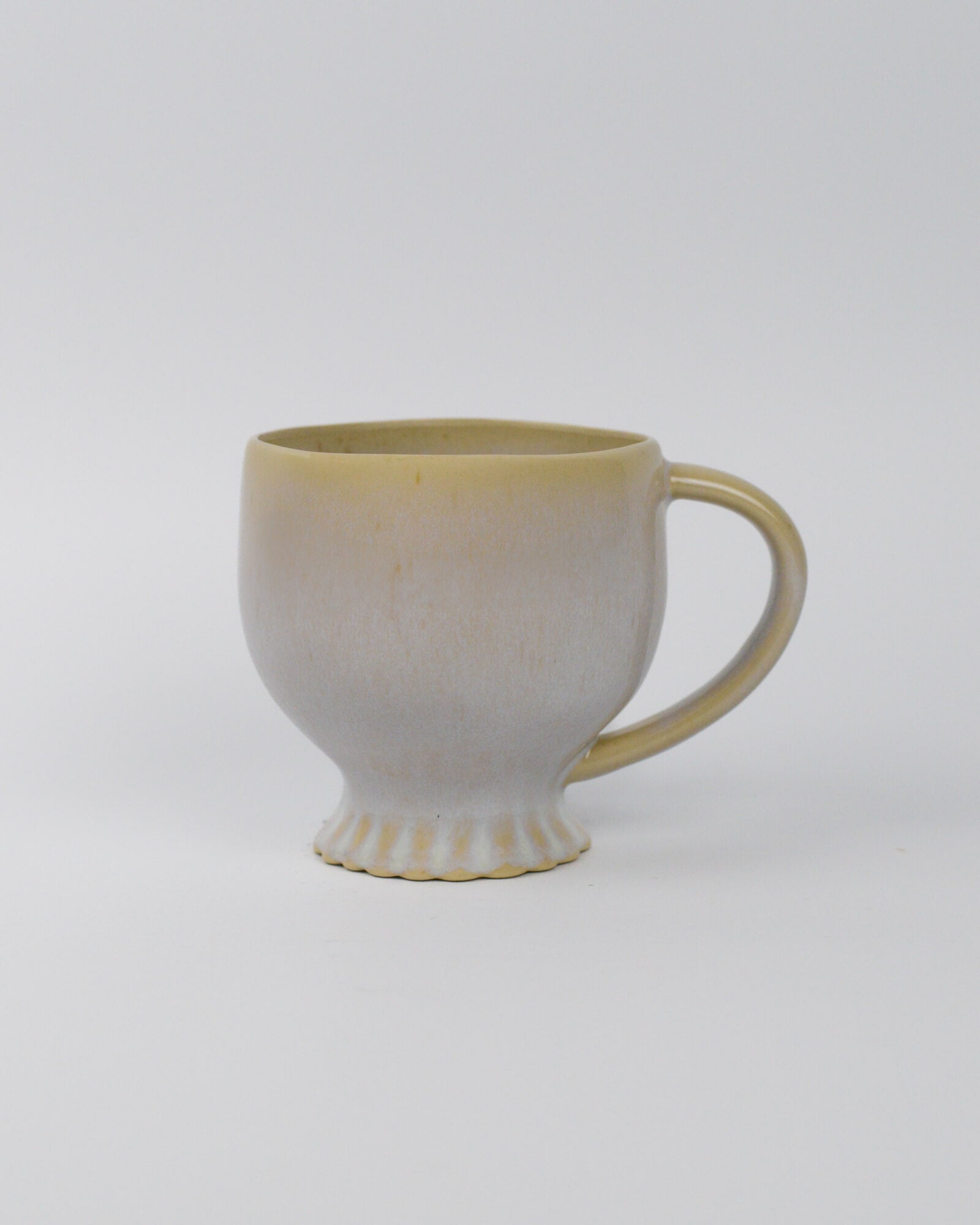 Ceramic mug with scalloped foot and a handle on a white background