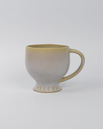 Ceramic mug with scalloped foot and a handle on a white background