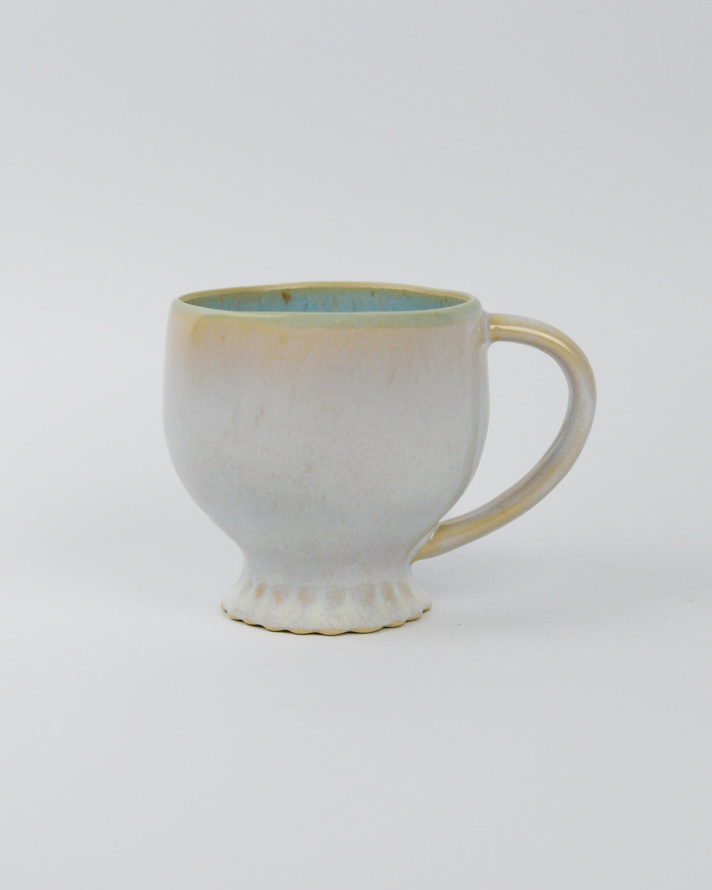 Ceramic mug with handle and scallopd foot and a textured surface on a white background